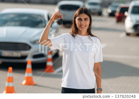 Smiling woman is standing and holding keys for her new car, on parking lot Smiling woman is standing and holding keys for her new car, on parking lot 137820248