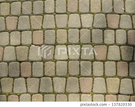 A fragment of a sidewalk paved with gray stone blocks with green stripes of sprouting grass, a beautiful abstract urban texture, the paved surface as an empty textured background. A fragment of a sidewalk paved with gray stone blocks with green stripes of sprouting grass, a beautiful abstract urban texture, the paved surface as an empty textured background. 137820330