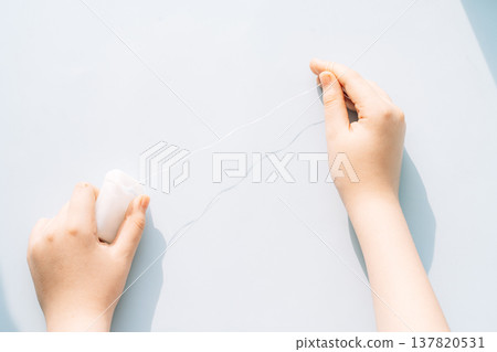 Child hands stretching dental floss from dispenser on light blue background, kids dental care routine Child hands stretching dental floss from dispenser on light blue background, kids dental care routine 137820531