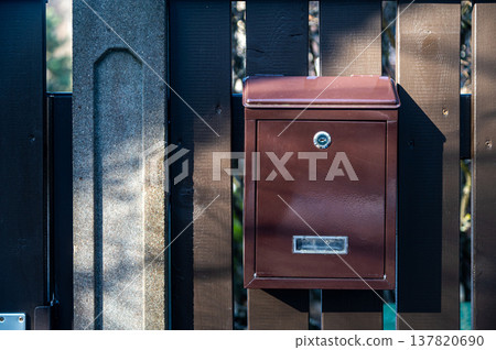 Brown mailbox mounted on wooden fence in residential area during daylight hours Brown mailbox mounted on wooden fence in residential area during daylight hours 137820690