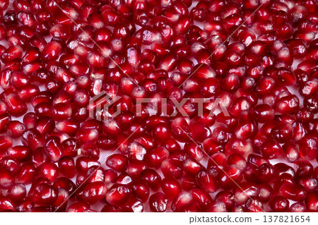 Close view of shiny pomegranate. Juicy pomegranate seeds with moist sheen in rustic setting. Seasonal bounty of saturated red pomegranate seeds gleaming in rustic victory 137821654