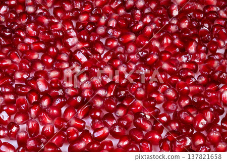 Natural light highlights scattered pomegranate arils with rich colors. Vivid pomegranate seeds spread across textured background emphasizing nutritious and appealing color scheme 137821658