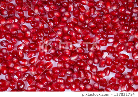 Colorful pomegranate seeds enhance culinary photography visuals beautifully. Bright red pomegranate seeds are scattered artistically across white surface for elegant menu display 137821754