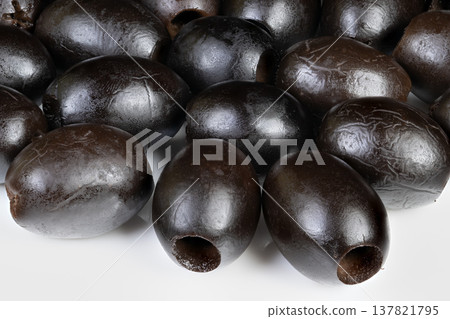 Olives on platter. Black olives with pits showcased. Closeup of moist black olives on white background. Arrangement of shiny black olives with pits on clean white surface Olives on platter. Black olives with pits showcased. Closeup of moist black olives on white background. Arrangement of shiny black olives with pits on clean white surface 137821795