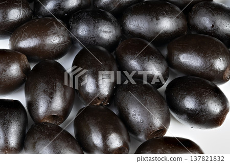Detailed view of glistening black olives arranged closely together. Highly detailed image of shiny black olives tightly packed against white background for product display 137821832