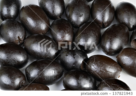 Tightly arranged shiny black olives on white background. Detailed image of oilglazed black olives carefully arranged against plain white backdrop for culinary presentation 137821943