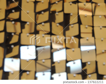 Shiny plastic golden squares suspended on strings as interior decor elements, holiday decorations in gold style with shimmering surface and geometric details in blurred focus 137822211