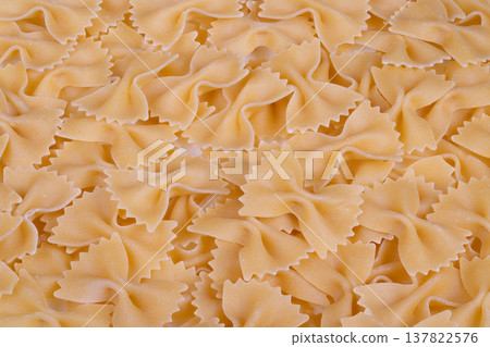 Spread of raw bowtie pasta. Unbaked bowtie shapes on kitchen surface. Scattered dry farfalle pasta pieces presenting appealing food styling for culinary imagery Spread of raw bowtie pasta. Unbaked bowtie shapes on kitchen surface. Scattered dry farfalle pasta pieces presenting appealing food styling for culinary imagery 137822576