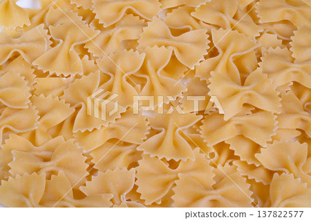 Closeup farfalle bowshaped pasta pile, dry uncooked pieces overlapping, warm beige semolina texture, subtle shadows, shallow depth of field, ideal background for food packaging Closeup farfalle bowshaped pasta pile, dry uncooked pieces overlapping, warm beige semolina texture, subtle shadows, shallow depth of field, ideal background for food packaging 137822577