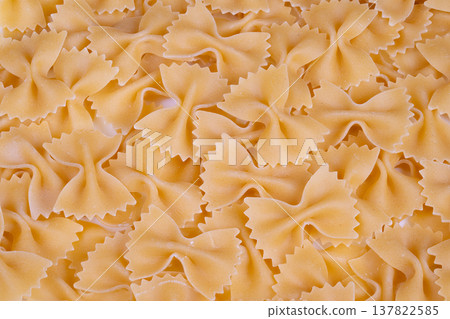 Overhead pile uncooked bowshaped pasta scatter, dense quantity with uniform shapes, matte semolina surface, cool studio lighting, texture study for packaging and commerce 137822585