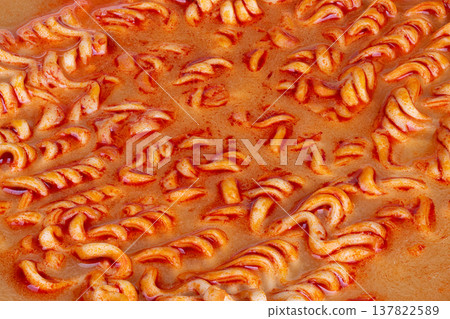Food stylist captures spicy steaming noodles. Vibrant red orange tones highlighting spicy instant meal. Closeup of glistening noodles with chili dust and steaming droplets 137822589
