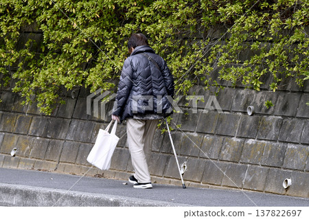 A picture of the cityscape of Yokohama, Japan...an elderly woman with a cane (wearing a mask) walking on the sidewalk with her head down...what is life...? = Yokohama city 137822697