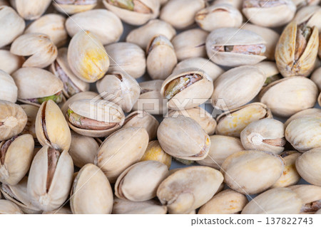 Roasted pistachios piled on display with cracked shells revealing toasted kernels, warm tones and crunchy appeal, evocative of snack stalls, gourmet shops, and food advertising Roasted pistachios piled on display with cracked shells revealing toasted kernels, warm tones and crunchy appeal, evocative of snack stalls, gourmet shops, and food advertising 137822743