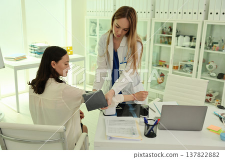 Nurse taking a patient's blood pressure during a routine check-up in a bright and modern clinic setting Nurse taking a patient's blood pressure during a routine check-up in a bright and modern clinic setting 137822882