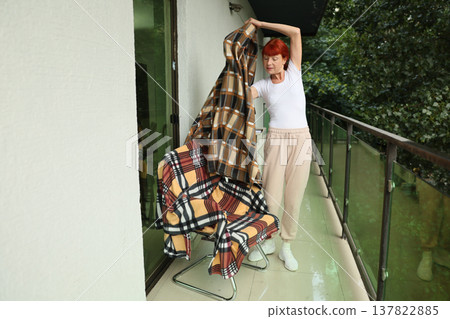 Woman arranging blankets on a balcony while enjoying a sunny day surrounded by greenery Woman arranging blankets on a balcony while enjoying a sunny day surrounded by greenery 137822885