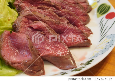 The vibrant pink slices of roast beef and fresh green lettuce are neatly arranged on a floral plate. The vibrant pink slices of roast beef and fresh green lettuce are neatly arranged on a floral plate. 137823046