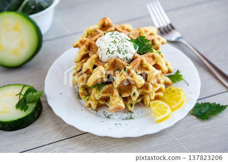 savory zucchini waffles with sour cream and fresh herbs on plate 137823206
