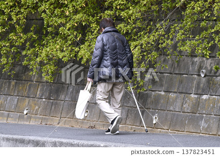 A picture of the cityscape of Yokohama, Japan...an elderly woman with a cane (wearing a mask) walking on the sidewalk with her head down...what is life...? = Yokohama city 137823451
