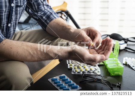 Middle aged caucasian man counts out pills for distributing scheduled dose of medication into pillbox Middle aged caucasian man counts out pills for distributing scheduled dose of medication into pillbox 137823513