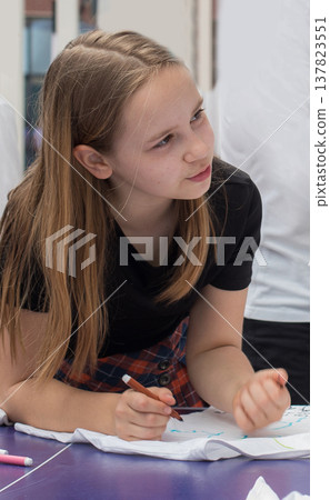 young girl student sitting at desk writing in notebook in school classroom. young girl student sitting at desk writing in notebook in school classroom. 137823551