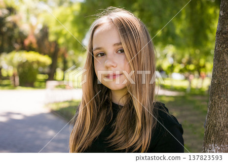 Cheerful little girl with long brown hair standing on summer nature park outdoors. Kid's portrait. Cheerful little girl with long brown hair standing on summer nature park outdoors. Kid's portrait. 137823593