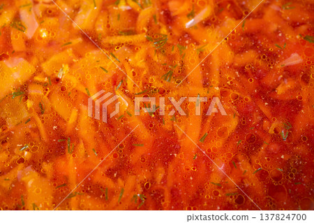 Hearty homemade soup. Comforting rustic borscht with potatoes and shimmering fat beads. Homemade beet and cabbage soup simmering in aged cast iron pot under warm kitchen light 137824700