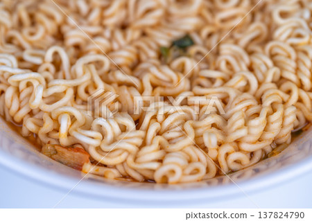 Shared instant noodles closeup with broth reflections and curled texture, suggests latenight snack or group sharing moment, warm tones and inviting composition Shared instant noodles closeup with broth reflections and curled texture, suggests latenight snack or group sharing moment, warm tones and inviting composition 137824790