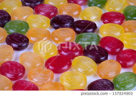 Colorful candy display. Display of vibrant hard candies laid flat with uniform spacing illuminated by professional studio lights for marketing and promotional materials Colorful candy display. Display of vibrant hard candies laid flat with uniform spacing illuminated by professional studio lights for marketing and promotional materials 137824903