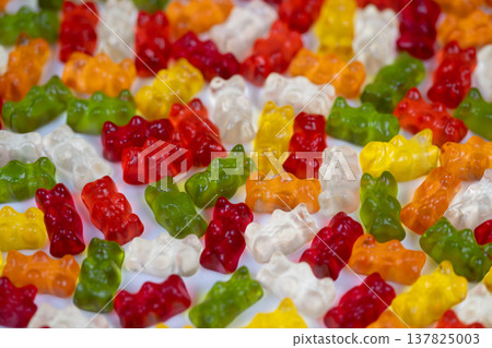 Colorful candy scene. Multicolored gummy bears focused tightly against white background. Sharp macro photograph featuring vibrantly colored gummy bears on plain white surface Colorful candy scene. Multicolored gummy bears focused tightly against white background. Sharp macro photograph featuring vibrantly colored gummy bears on plain white surface 137825003
