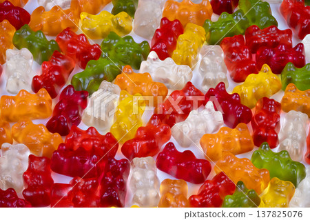 Brightly colored candies dispersed on plain surface. An assortment of vividly hued gummy bears spread over white platform with gentle shadow effects for visual presentations Brightly colored candies dispersed on plain surface. An assortment of vividly hued gummy bears spread over white platform with gentle shadow effects for visual presentations 137825076