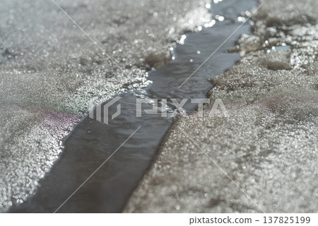 Path of flowing meltwater through snow with textures and lines. Meandering meltwater stream carving through snow with visible current patterns and contrasting textures 137825199