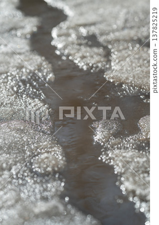 Calm winter water surface adorned with delicate oscillations and shining highlights. Tranquil icy waterway displaying subtle waves and reflective gleams during seasonal change 137825219