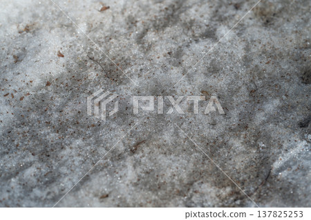 Dirty spring snow granular and glistening, surface pocked with dark grit and oil specks, macro view of icy melt on urban pavement, cool highlights and gritty industrial mood 137825253