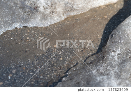 Frozen border highlights asphalt surface with subtle texture changes. Illuminated frost edge uncovers underlying asphalt with varying textures and gentle slopes 137825409