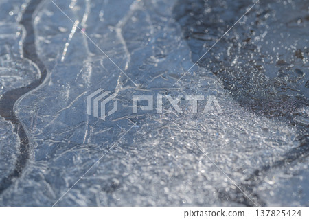 Melting ice patterns. Spring ice exhibits flowing textures. Ice thaws in spring revealing elegant flow. Melting snow showcases gentle flowing designs and shiny surfaces Melting ice patterns. Spring ice exhibits flowing textures. Ice thaws in spring revealing elegant flow. Melting snow showcases gentle flowing designs and shiny surfaces 137825424