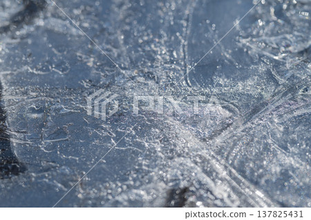 Elaborate network of fractures on shimmering spring ice surface. Intricate fracture formations displaying shimmering reflections and detailed vein structures on springtime ice 137825431
