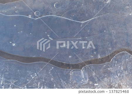 Ice featuring trapped air bubbles and distinctive circular indentations on its surface. Translucent frozen water surface showing embedded air pockets and circular impressions 137825468
