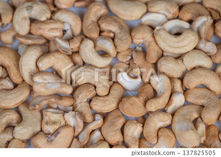Golden brown nut pattern. Detailed photograph showcasing crispy roasted nut textures. Closeup macro shot capturing warm tones and textured surfaces of roasted cashews Golden brown nut pattern. Detailed photograph showcasing crispy roasted nut textures. Closeup macro shot capturing warm tones and textured surfaces of roasted cashews 137825505