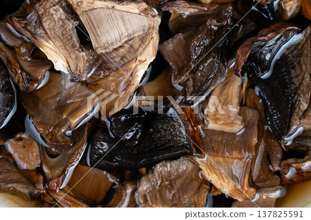 Dried fungi submerged creating savory infusion for culinary use. Rehydrating dried mushrooms releases concentrated savory notes for soups and sauces preparation 137825591