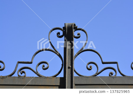 Ornamental wrought iron fence scrollwork against blue sky 137825965
