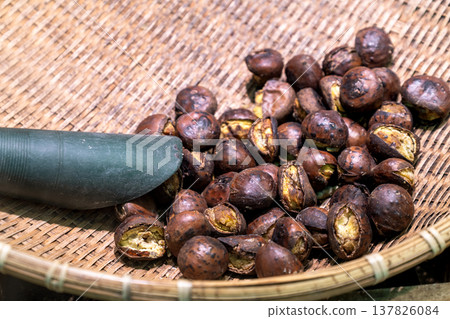 Roasted chestnuts in a woven bamboo basket with a metal scoop. Traditional Asian street food snack. High angle view of peeled and unpeeled nuts with cracked shells on a wooden tray background. Roasted chestnuts in a woven bamboo basket with a metal scoop. Traditional Asian street food snack. High angle view of peeled and unpeeled nuts with cracked shells on a wooden tray background. 137826084