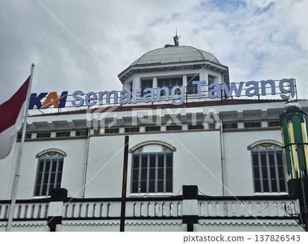The historic Semarang Tawang Railway Station in Indonesia features magnificent Dutch colonial architecture with its iconic large dome and vintage windows under a dramatic cloudy afternoon sky. 137826543