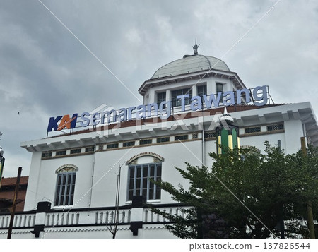 The historic Semarang Tawang Railway Station in Indonesia features magnificent Dutch colonial architecture with its iconic large dome and vintage windows under a dramatic cloudy afternoon sky. The historic Semarang Tawang Railway Station in Indonesia features magnificent Dutch colonial architecture with its iconic large dome and vintage windows under a dramatic cloudy afternoon sky. 137826544