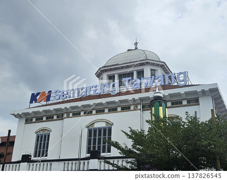 The historic Semarang Tawang Railway Station in Indonesia features magnificent Dutch colonial architecture with its iconic large dome and vintage windows under a dramatic cloudy afternoon sky. The historic Semarang Tawang Railway Station in Indonesia features magnificent Dutch colonial architecture with its iconic large dome and vintage windows under a dramatic cloudy afternoon sky. 137826545