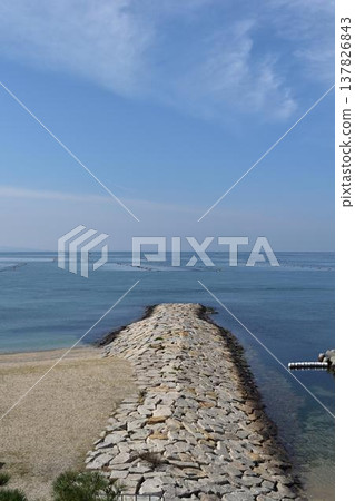 一道石砌防波堤垂直橫跨沙灘和寧靜的大海。 一道石砌防波堤垂直橫跨沙灘和寧靜的大海。 137826843