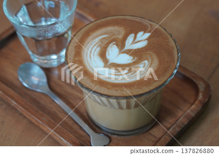 side view brown coffee and milk in low glass on wooden tray, silver spoon and water in glass, brown wooden floor background, drink, cool, food, copy space 137826880