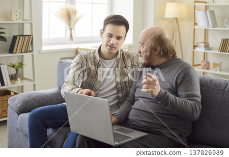 Adult son teaching his mature father how to use laptop computer, explaining something  137826989