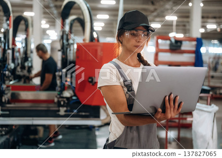 Laptop is in hands. Woman is in the window making factory 137827065