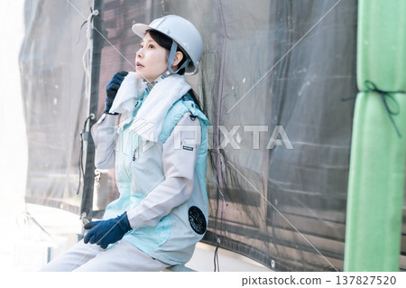 [Safety and Hygiene] A female painter resting in the shade and recovering her strength, wearing a cooling vest. 137827520