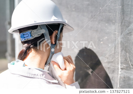 The reality of the scene. Sweat glistens on the nape of the neck of a female worker supporting a home renovation in the scorching heat. The reality of the scene. Sweat glistens on the nape of the neck of a female worker supporting a home renovation in the scorching heat. 137827521